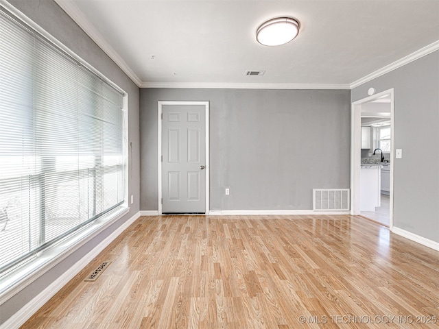 spare room featuring crown molding, baseboards, visible vents, and light wood-type flooring