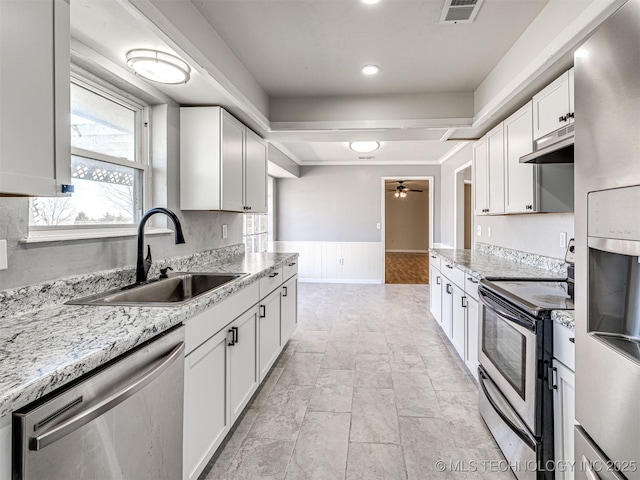 kitchen with visible vents, a sink, under cabinet range hood, wainscoting, and appliances with stainless steel finishes