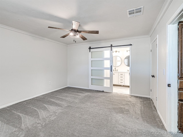 spare room with a barn door, carpet flooring, visible vents, and ornamental molding