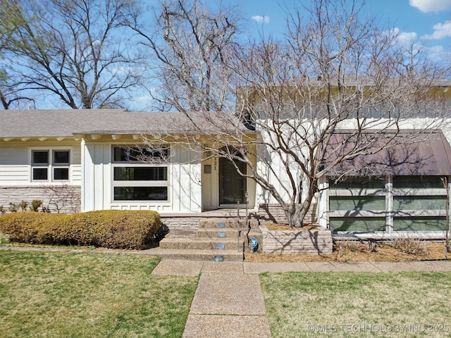 view of front facade with a front yard, board and batten siding, and a shingled roof