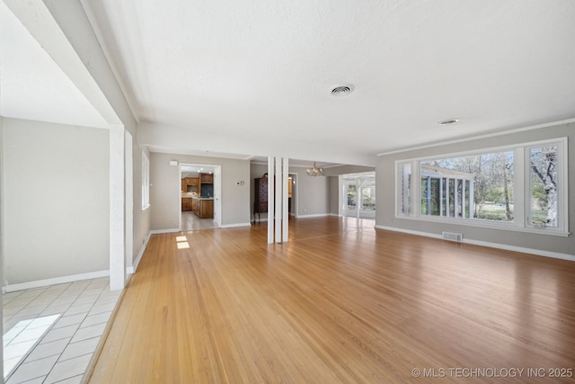 unfurnished living room featuring baseboards, light wood-style floors, visible vents, and a chandelier
