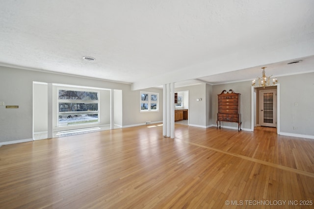 unfurnished living room featuring visible vents, light wood-style flooring, a textured ceiling, baseboards, and a chandelier