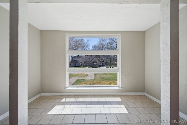 empty room with baseboards, light tile patterned flooring, and a textured wall