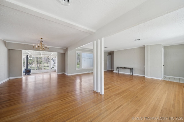 unfurnished living room with a notable chandelier, light wood-style flooring, a textured ceiling, and baseboards