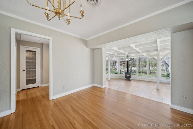 empty room featuring a wood stove, wood finished floors, visible vents, and baseboards