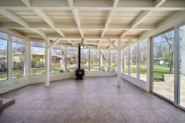 unfurnished sunroom with a ceiling fan, coffered ceiling, a wood stove, tile patterned flooring, and beamed ceiling