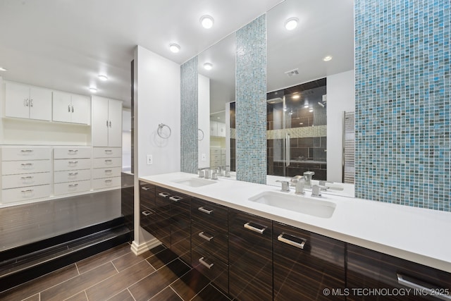 full bathroom with a sink, visible vents, tiled shower, and double vanity