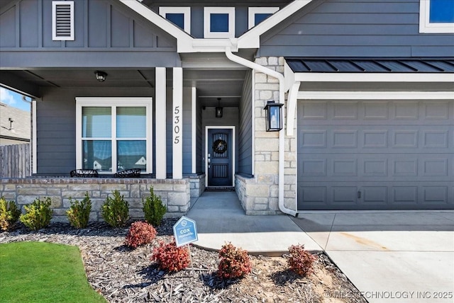 doorway to property with covered porch, concrete driveway, a garage, stone siding, and board and batten siding