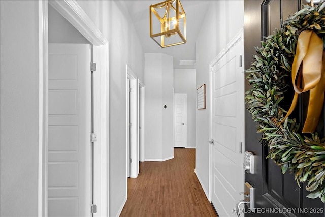 hallway featuring a notable chandelier, baseboards, and wood finished floors