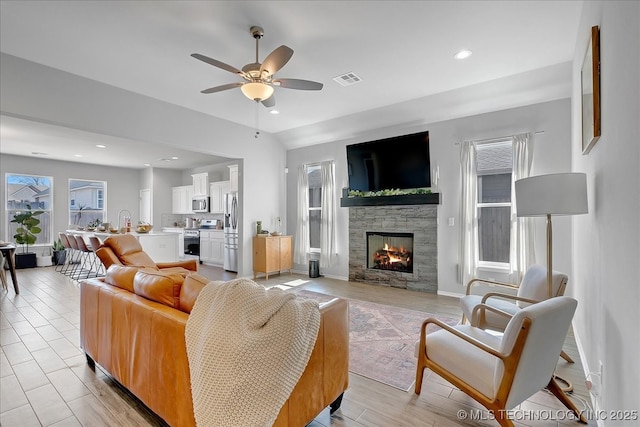 living area with recessed lighting, visible vents, a stone fireplace, and a ceiling fan