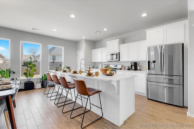 kitchen featuring backsplash, a center island with sink, a kitchen bar, light countertops, and appliances with stainless steel finishes