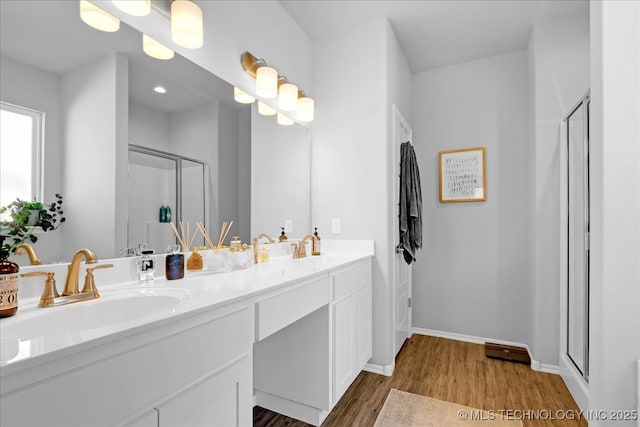 bathroom featuring a stall shower, a sink, wood finished floors, double vanity, and baseboards