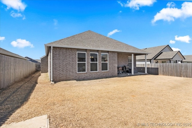 rear view of house with a patio area, brick siding, a fenced backyard, and a shingled roof