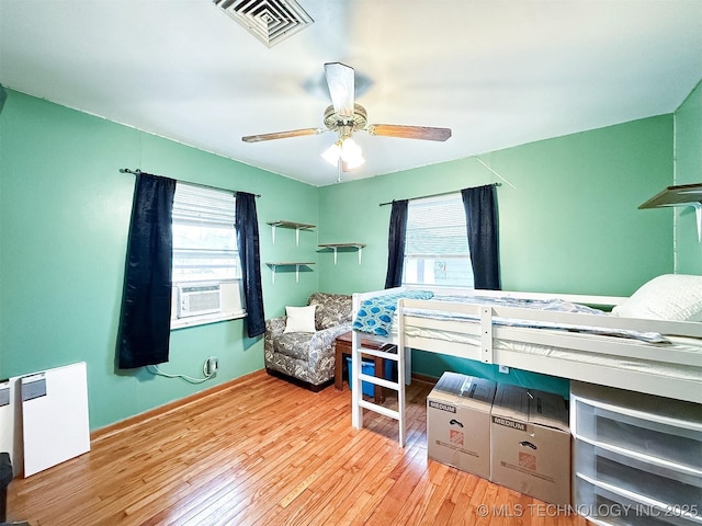 bedroom with multiple windows, cooling unit, visible vents, and wood-type flooring