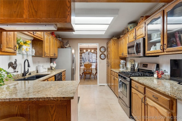 kitchen featuring light stone countertops, appliances with stainless steel finishes, an inviting chandelier, brown cabinetry, and a sink