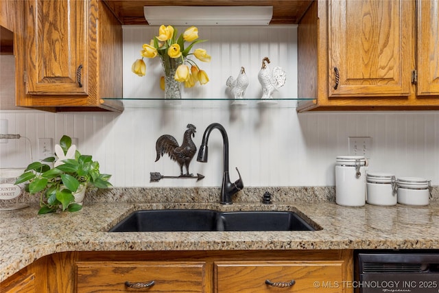 kitchen with light stone countertops, brown cabinets, and a sink