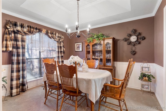 dining space with crown molding, light colored carpet, a tray ceiling, wainscoting, and a notable chandelier