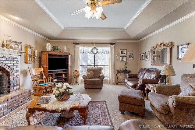 carpeted living room featuring a raised ceiling, a brick fireplace, a ceiling fan, and crown molding