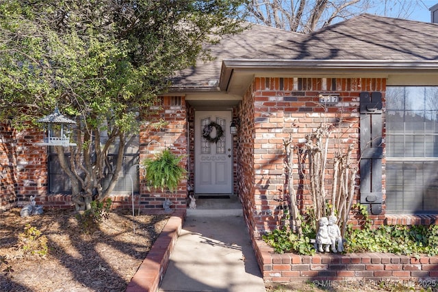 view of exterior entry featuring brick siding and a shingled roof