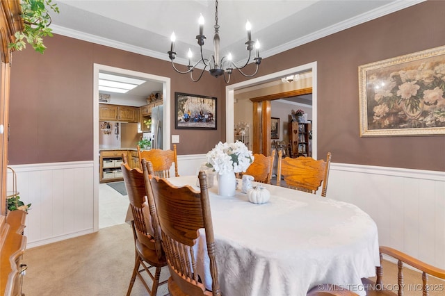 dining room featuring an inviting chandelier, light carpet, crown molding, and wainscoting