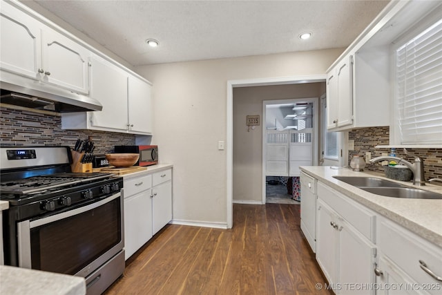 kitchen featuring a sink, under cabinet range hood, stainless steel gas stove, white cabinetry, and dark wood-style flooring