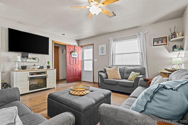 living room with visible vents, ceiling fan, light wood-type flooring, a fireplace, and a textured ceiling