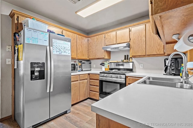 kitchen featuring under cabinet range hood, a sink, stainless steel appliances, light wood finished floors, and light countertops