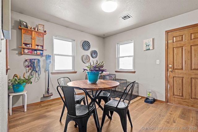 dining room featuring a textured ceiling, light wood-style floors, visible vents, and baseboards