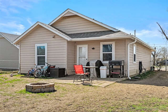 rear view of house with fence, a fire pit, a shingled roof, and a patio area