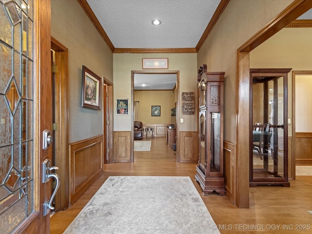 foyer featuring a textured ceiling, light wood-style flooring, ornamental molding, and wainscoting