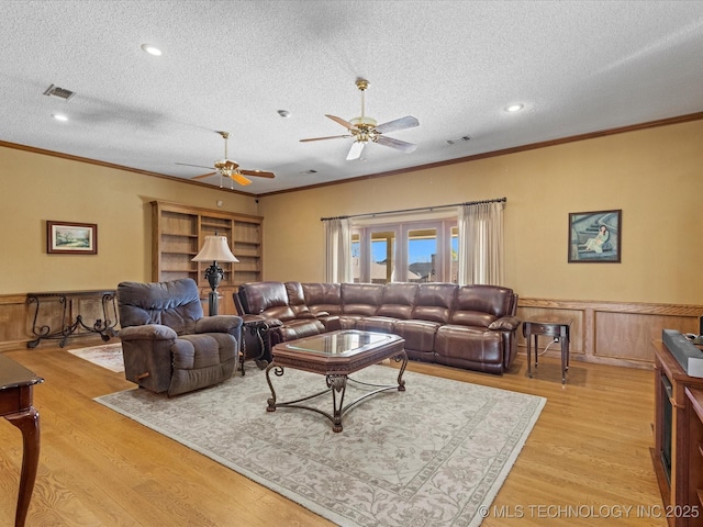 living area featuring visible vents, light wood finished floors, a ceiling fan, crown molding, and wainscoting