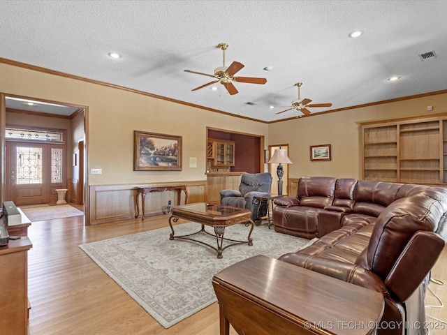 living area featuring a ceiling fan, a wainscoted wall, visible vents, light wood-style floors, and a textured ceiling