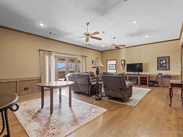 living room featuring ornamental molding, ceiling fan, wainscoting, and light wood finished floors