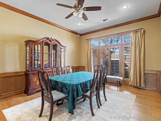 dining room featuring visible vents, light wood-style flooring, crown molding, and a wainscoted wall