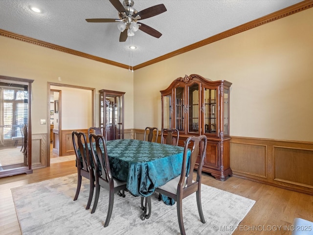 dining area featuring a wainscoted wall, a textured ceiling, light wood-style floors, crown molding, and ceiling fan