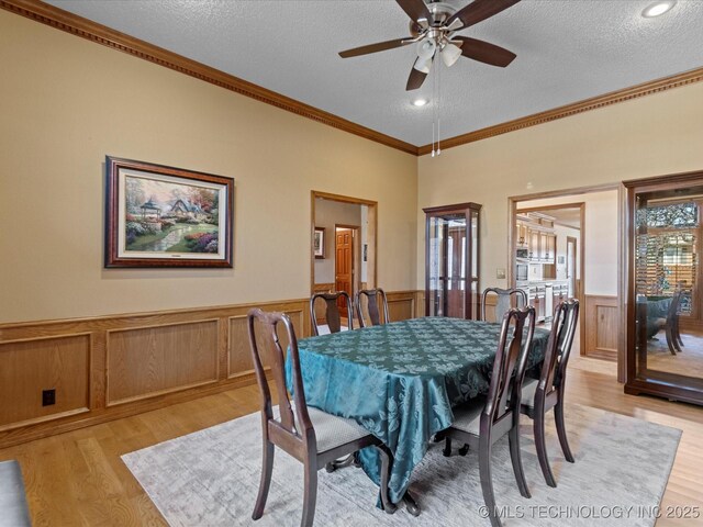 dining area featuring a wainscoted wall, a textured ceiling, light wood-type flooring, and a ceiling fan