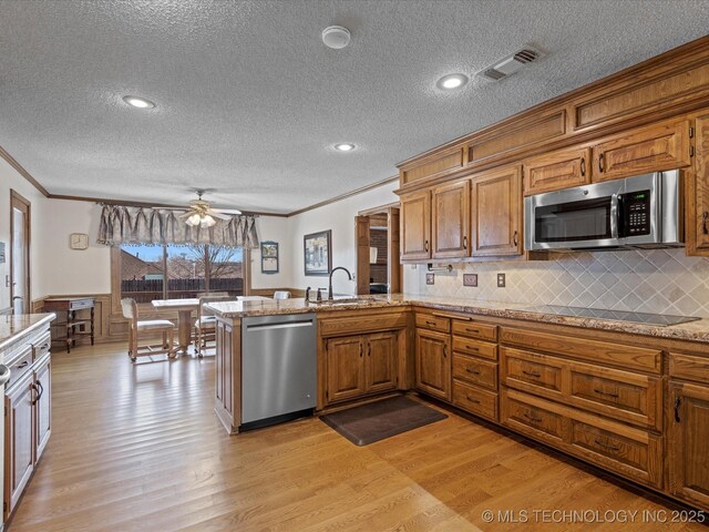 kitchen featuring visible vents, light wood-style flooring, a peninsula, stainless steel appliances, and a sink