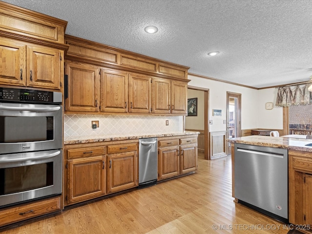 kitchen with light wood-style flooring, brown cabinets, appliances with stainless steel finishes, and wainscoting