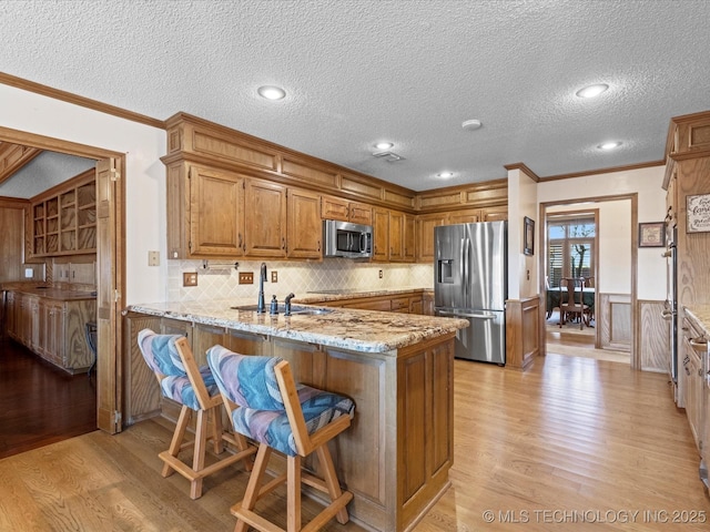 kitchen featuring brown cabinetry, a peninsula, a sink, stainless steel appliances, and wainscoting