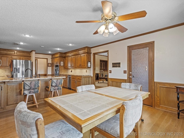 dining room with a textured ceiling, ornamental molding, wainscoting, and light wood finished floors