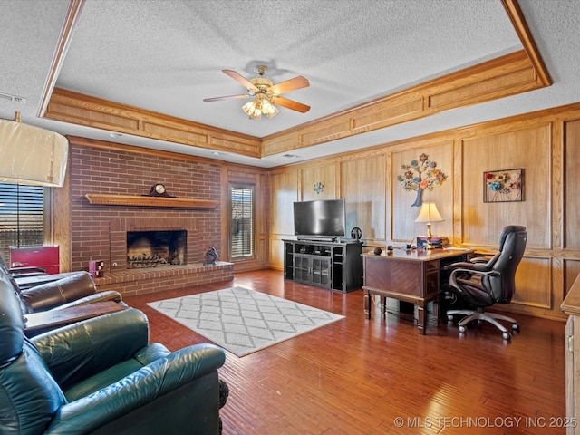 living area with a textured ceiling, a raised ceiling, a ceiling fan, and wood finished floors