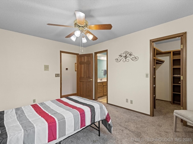 bedroom featuring light carpet, a textured ceiling, baseboards, ceiling fan, and a spacious closet