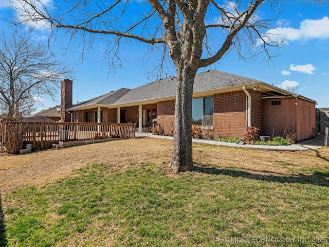 back of house featuring a yard, brick siding, roof with shingles, and a deck