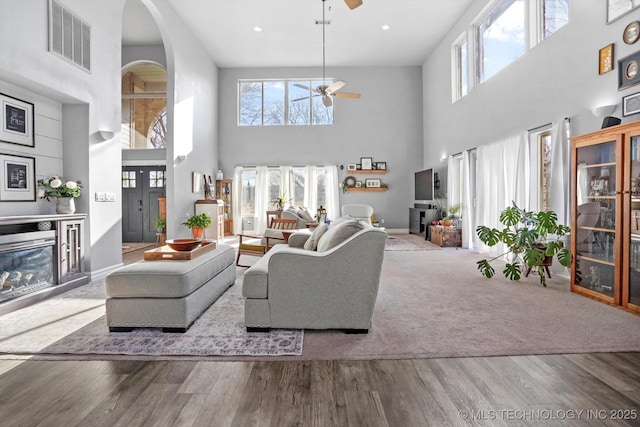 living area featuring wood finished floors, a ceiling fan, visible vents, and arched walkways