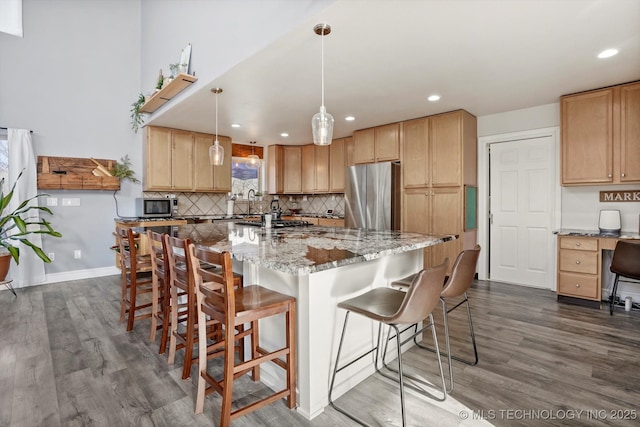 kitchen with tasteful backsplash, dark wood finished floors, a center island with sink, light stone counters, and appliances with stainless steel finishes