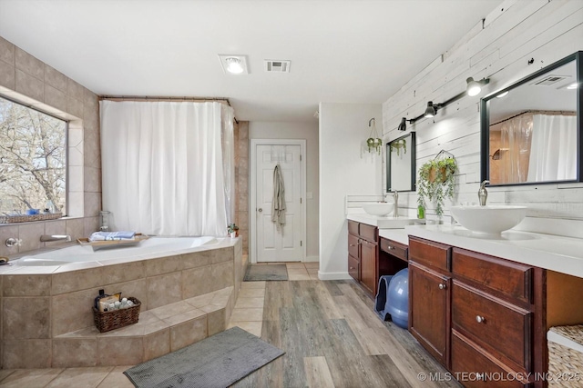 full bathroom featuring wood finished floors, visible vents, double vanity, a sink, and a garden tub