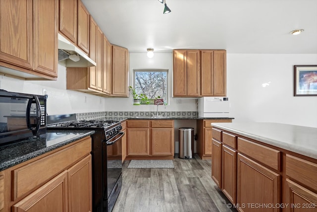 kitchen featuring black appliances, light wood-style flooring, under cabinet range hood, a sink, and brown cabinetry