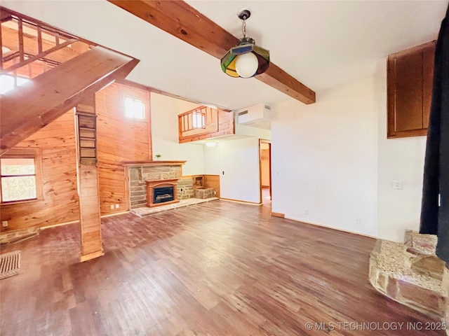 unfurnished living room with beam ceiling, wooden walls, a stone fireplace, and wood finished floors