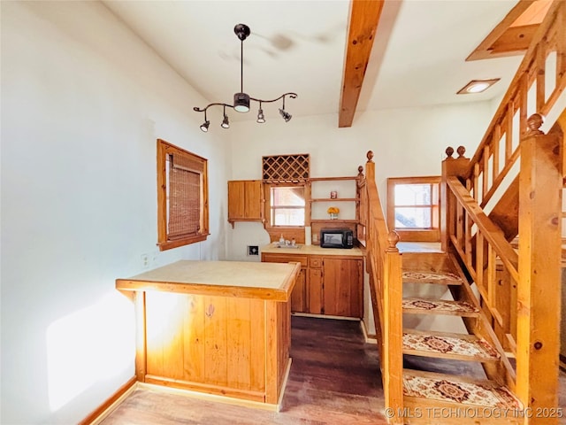 kitchen featuring wood finished floors, baseboards, a peninsula, beam ceiling, and light countertops