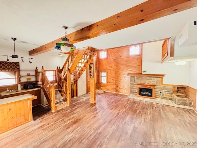 living area with stairway, wooden walls, wood finished floors, beam ceiling, and a fireplace